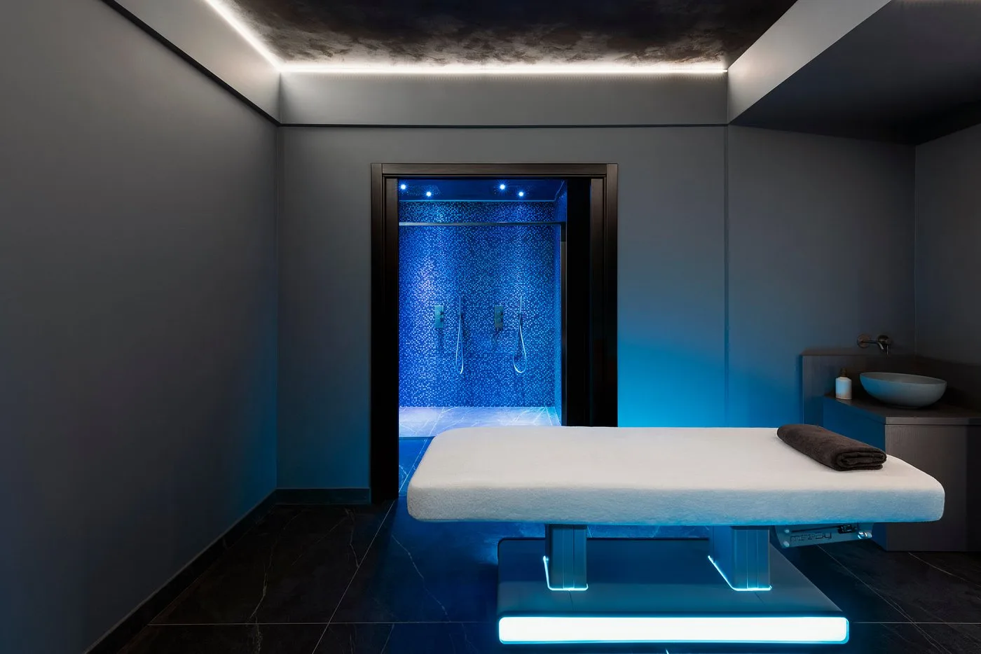 Sala massaggi della spa con lettino e doccia emozionale illuminata di blu