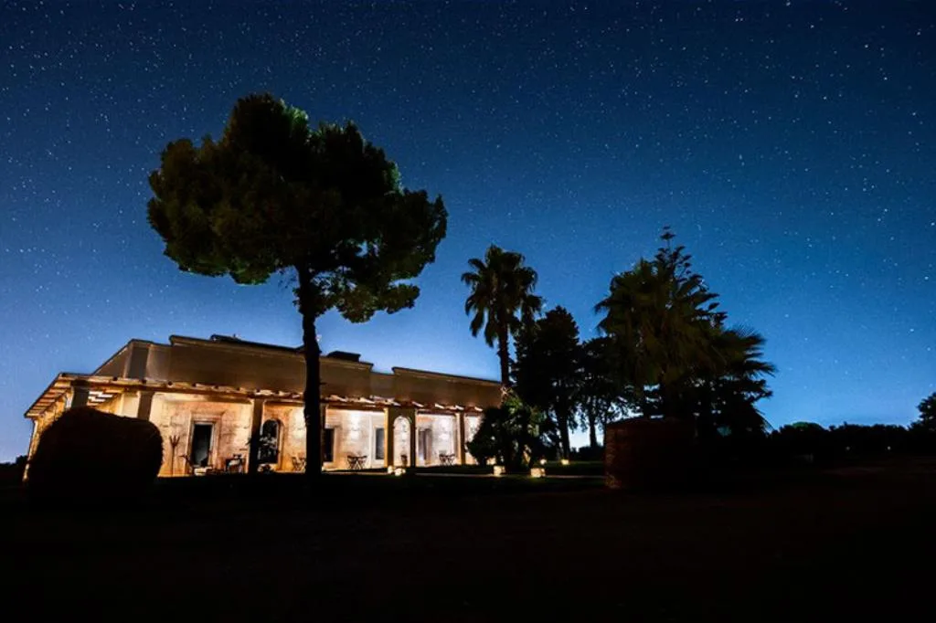 Masseria illuminata di notte sotto un cielo stellato con pini e palme
