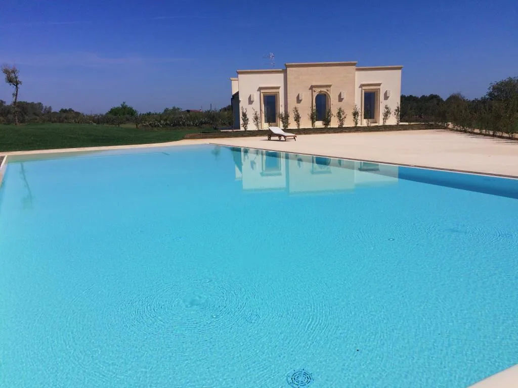 Grande piscina azzurra con la villa in pietra riflessa sullo sfondo