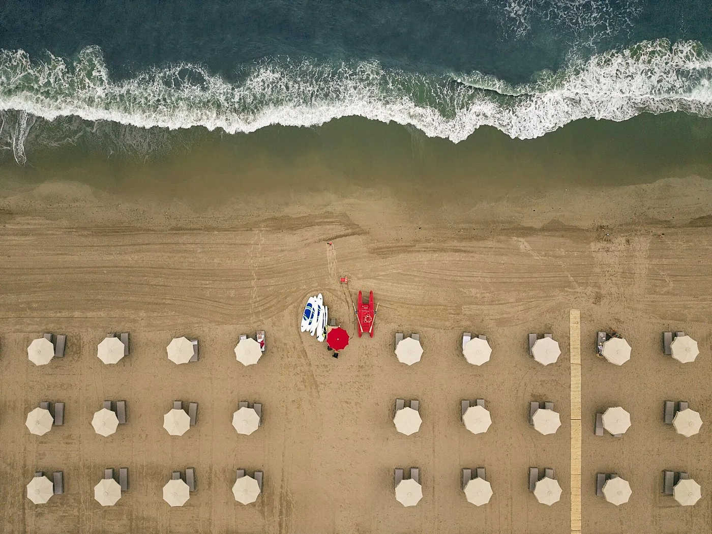 Veduta aerea della spiaggia con ombrelloni ordinati e onde del mare