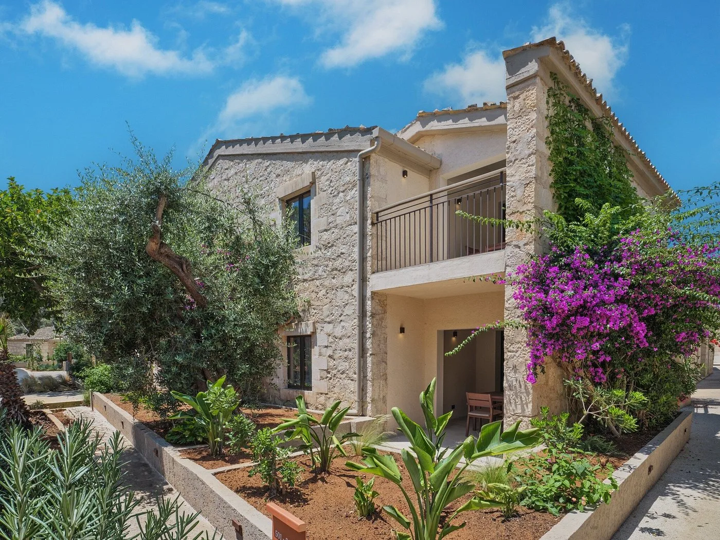 Edificio in pietra a due piani con balcone, giardino e bougainvillea fiorita