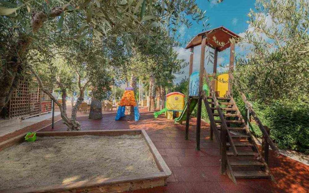 Parco giochi per bambini con scivoli colorati e sabbiera tra gli ulivi