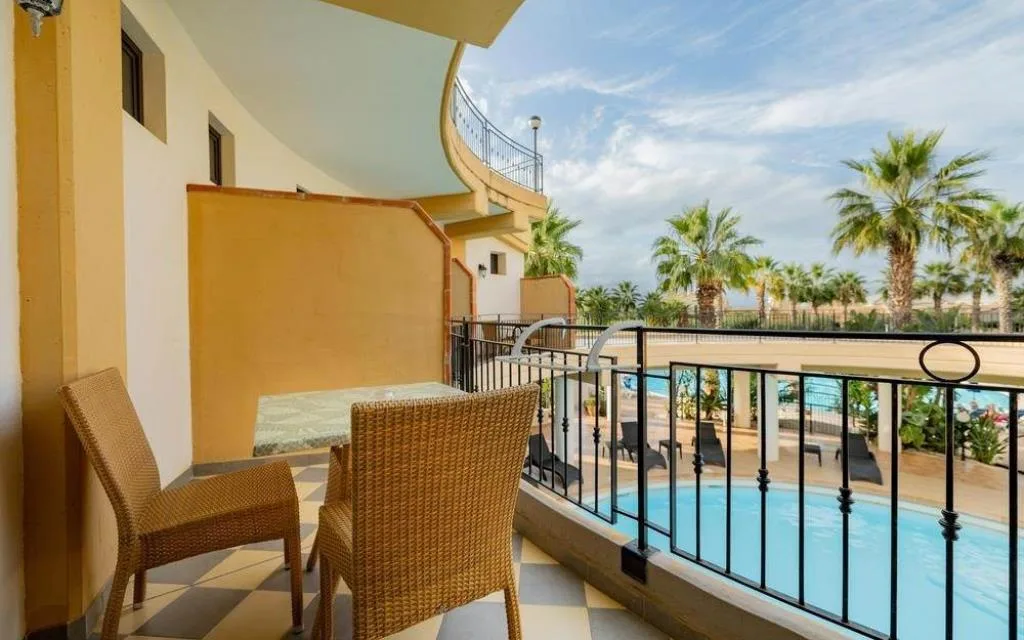 Balcone con tavolino e sedie in rattan affacciato sulla piscina e palme