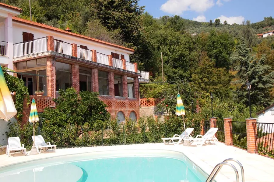 Piscina con lettini e ombrelloni davanti a villa in mattoni immersa nel verde