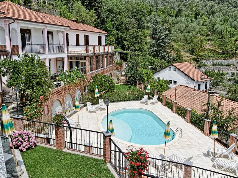 Vista dall'alto della villa con piscina, giardino fiorito e colline boscose