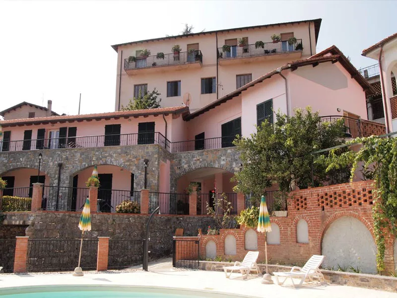 Facciata dell'edificio rosa con portici in pietra e piscina con ombrelloni in primo piano