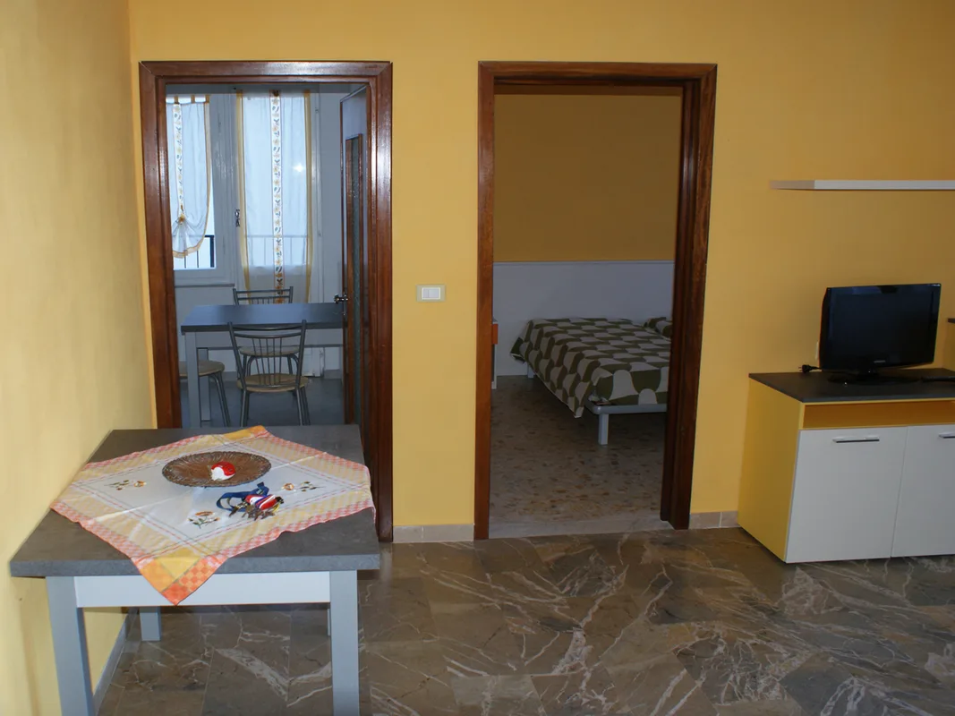 Soggiorno giallo con TV, tavolo e vista su camera matrimoniale e zona pranzo