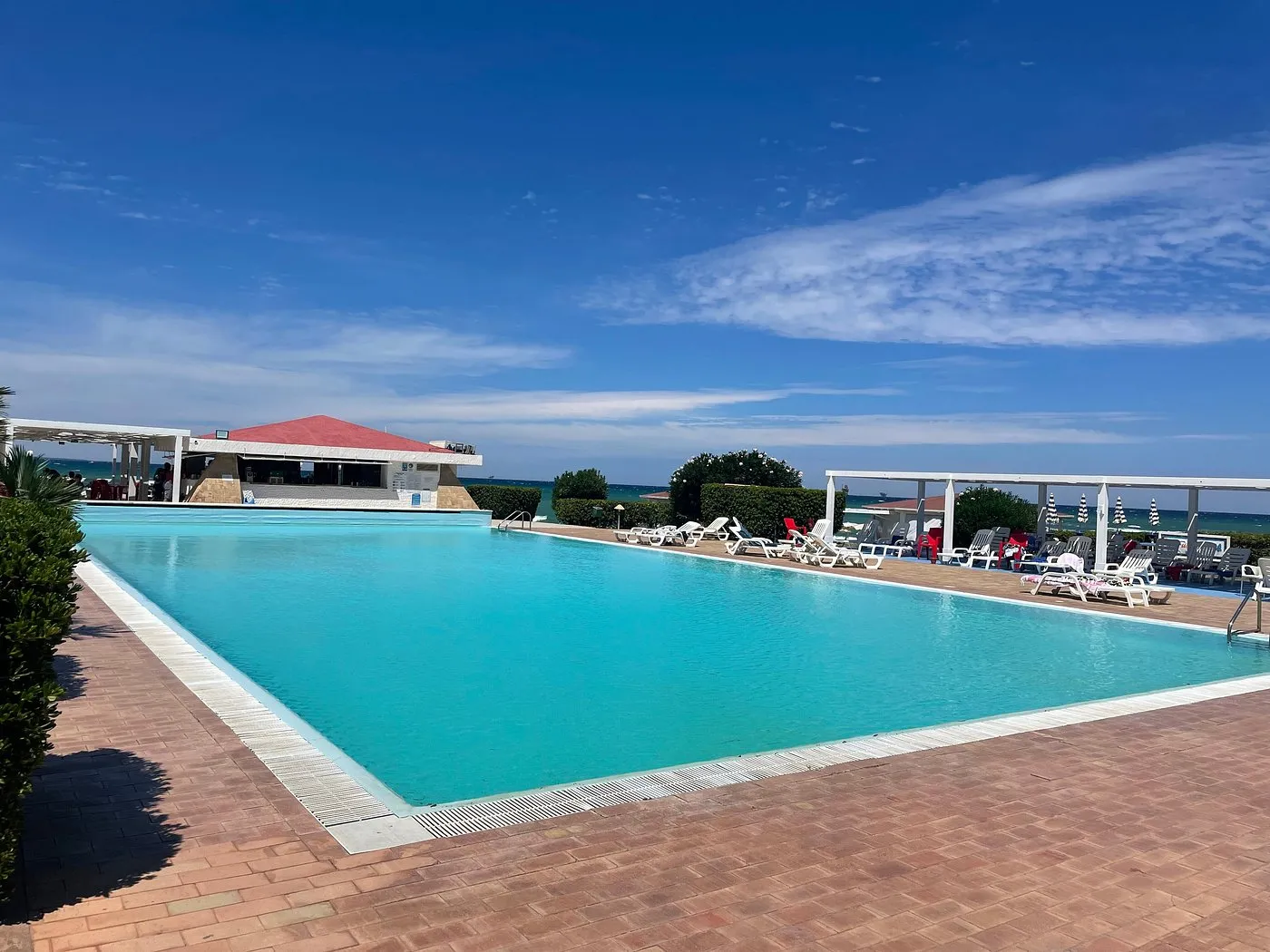 Grande piscina rettangolare con lettini, pergolati bianchi e vista sul mare