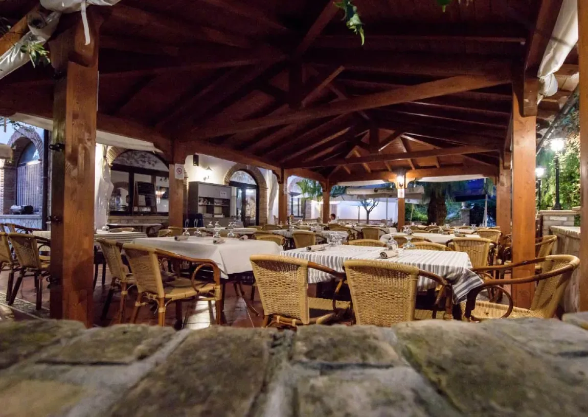 Ristorante interno con travi in legno, tavoli apparecchiati e sedie in vimini