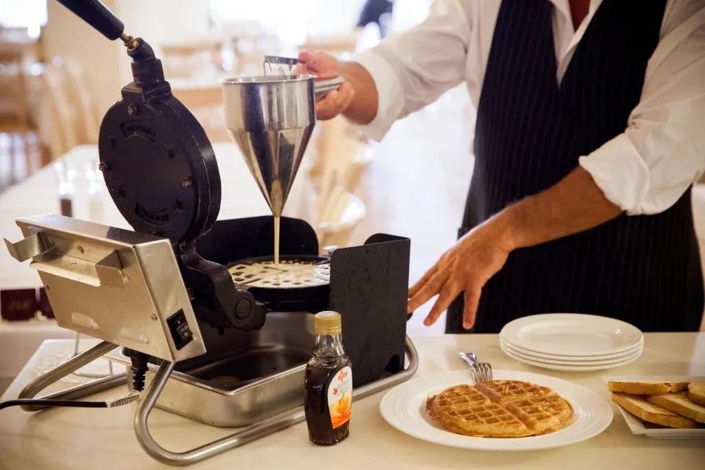 Cameriere prepara waffle fresche con macchina apposita durante la colazione
