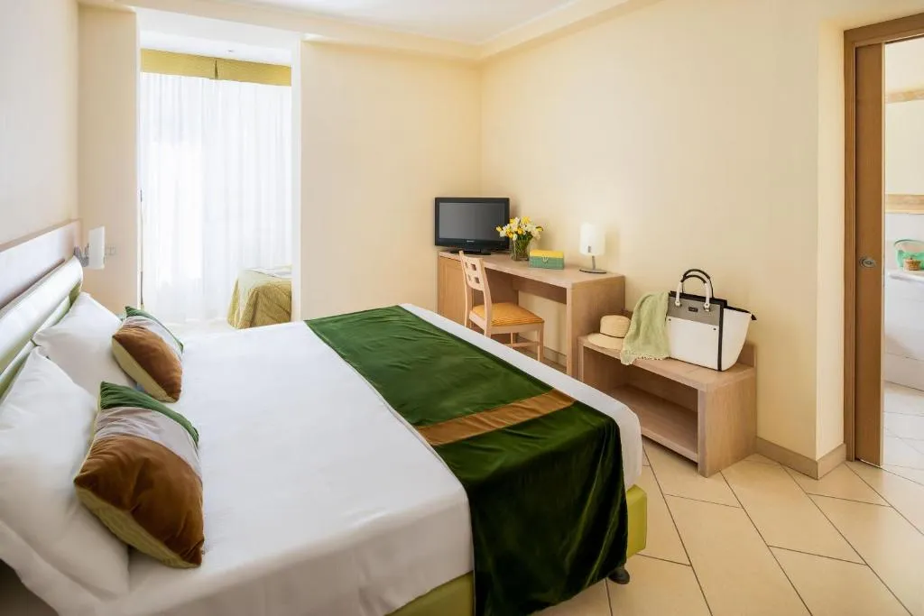 Camera con letto matrimoniale, copriletto verde, scrivania e TV