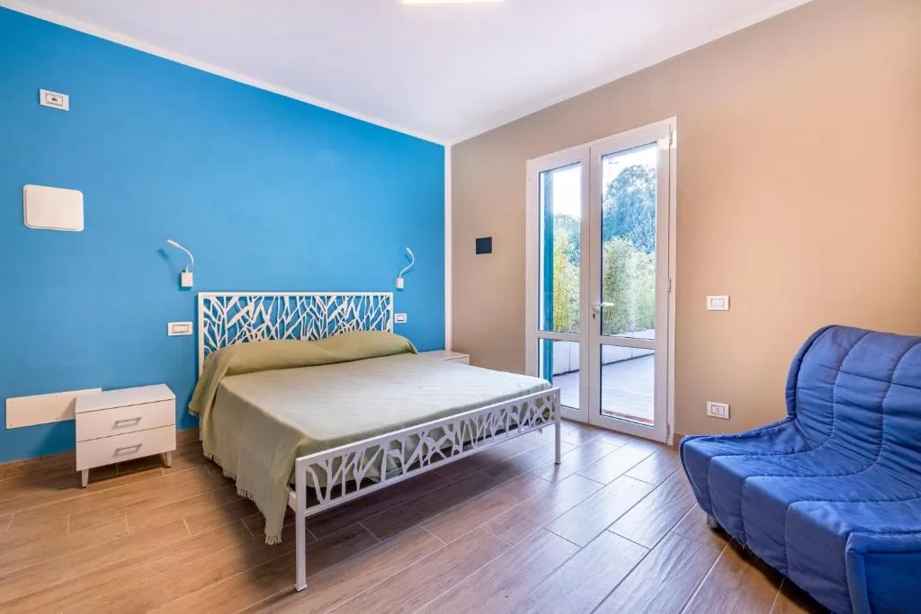 Camera da letto con parete blu, letto matrimoniale, poltrona blu e porta finestra