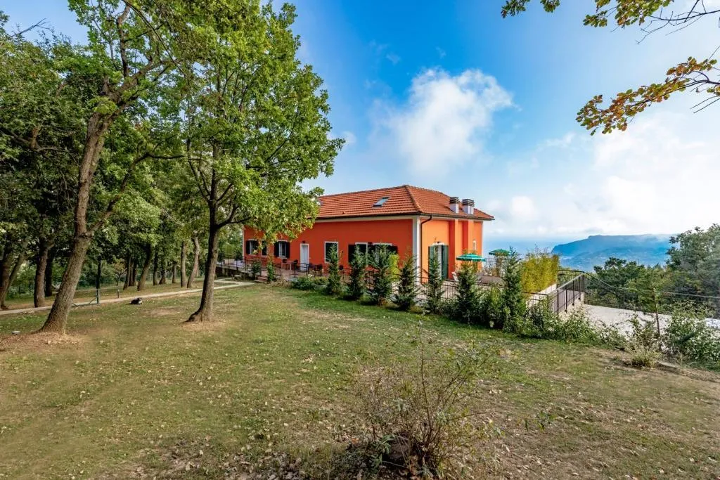 Villa arancione con tetto rosso circondata da alberi e prato verde