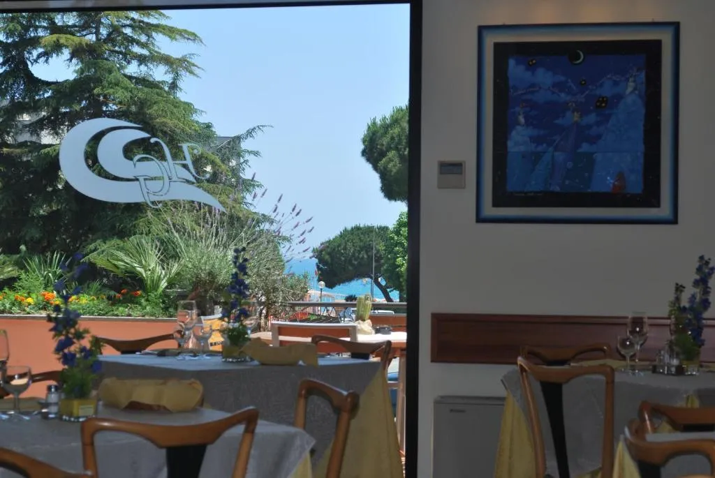 Sala ristorante con tavoli apparecchiati e vista sul giardino e sul mare