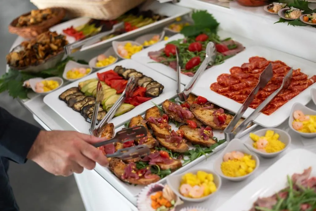 Buffet con vassoi di verdure grigliate, salumi e bruschette servito con pinze