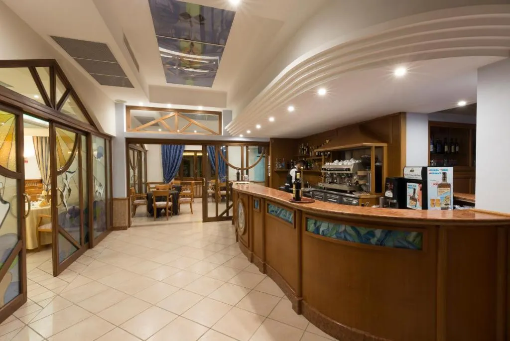 Bar dell'hotel con bancone in legno, macchina del caffè e sala adiacente con tavoli