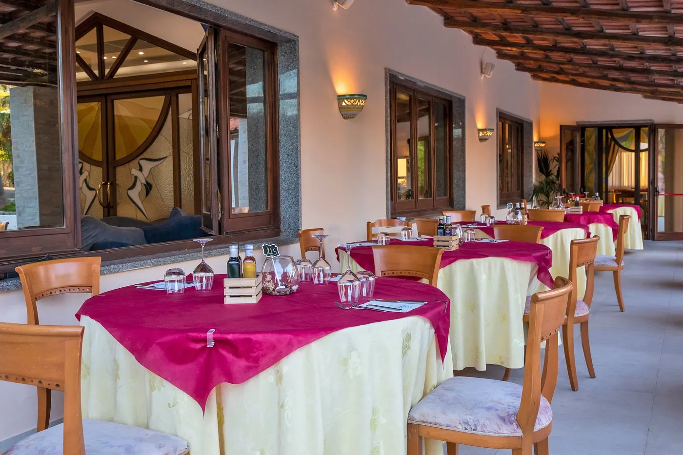 Terrazza ristorante con tavoli apparecchiati, tovaglie fucsia e gialle e soffitto in legno