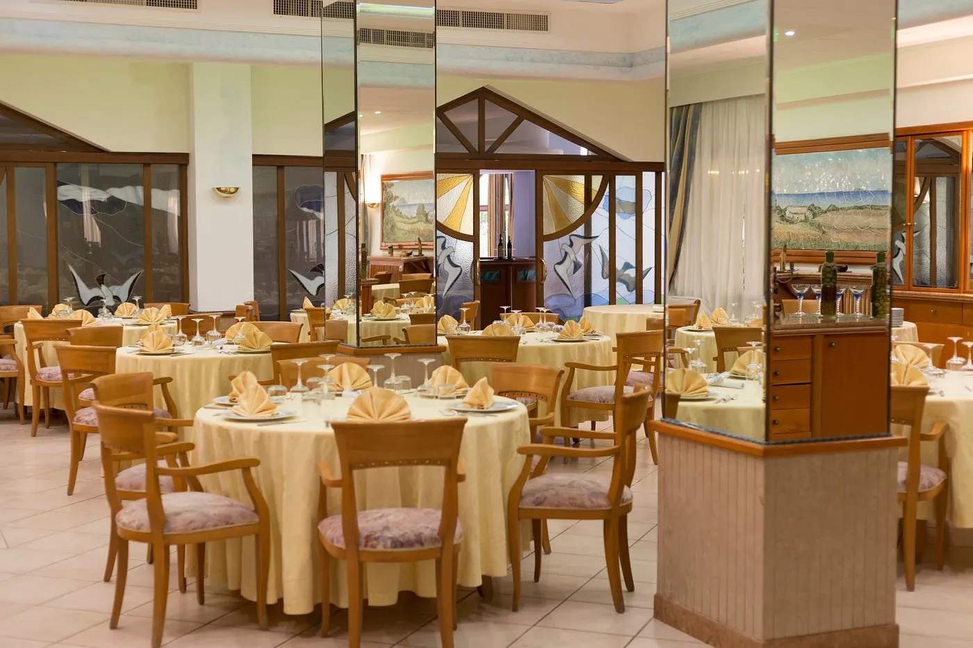 Sala ristorante interna con tavoli rotondi apparecchiati, tovaglie gialle e vetrate decorate