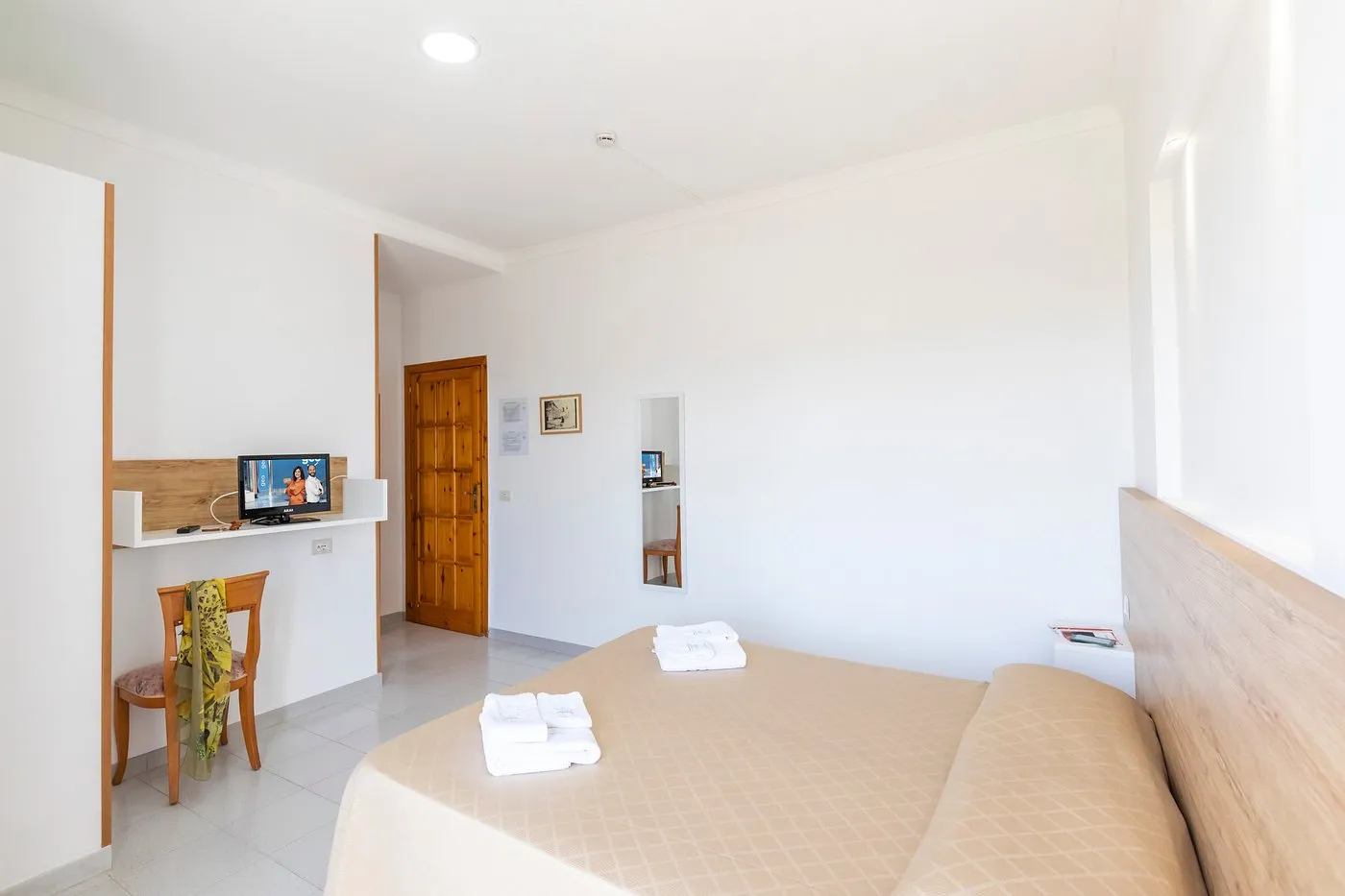 Camera matrimoniale con scrivania, TV, sedia e ampie pareti bianche luminose