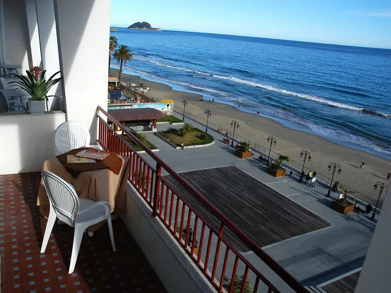 Balcone con tavolino e sedie bianche affacciato sul mare, lungomare e spiaggia