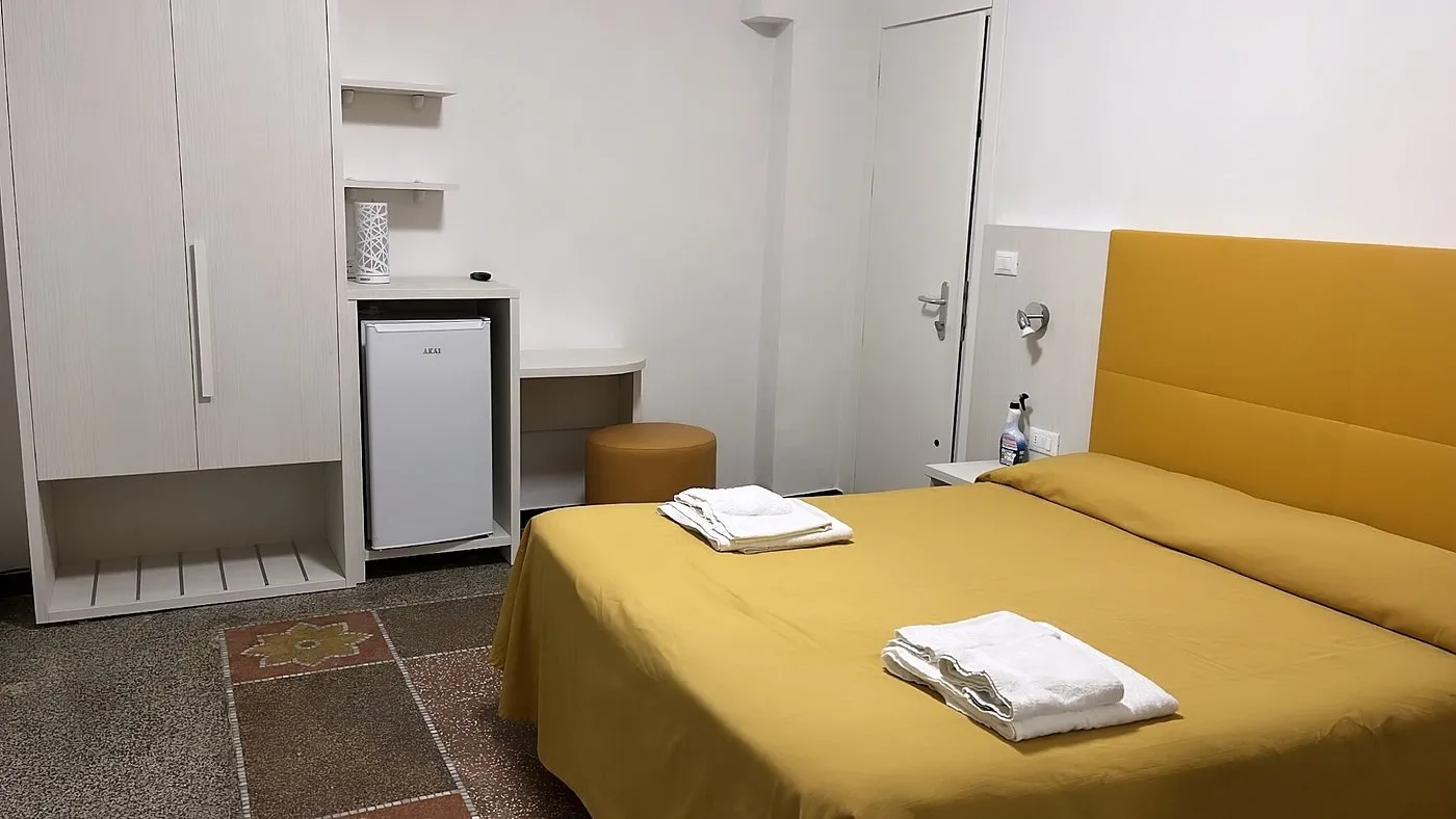 Camera con letto matrimoniale, armadio bianco e minifrigo