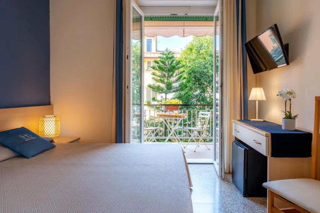 Camera con porta finestra aperta su balcone con tavolino e vista alberi