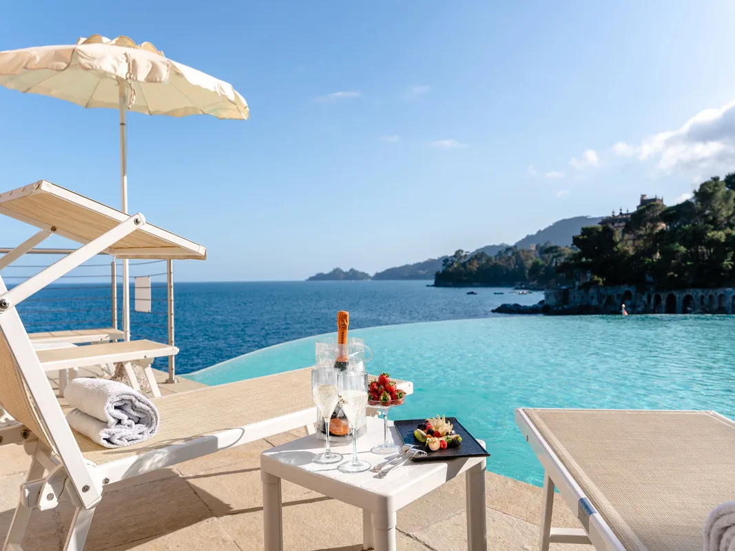Lettini e ombrellone a bordo piscina con prosecco e fragole vista mare