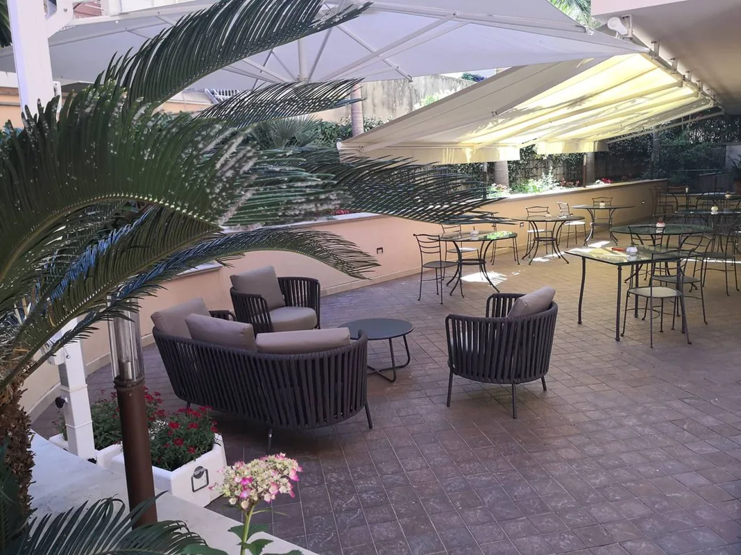 Terrazza esterna con poltrone, tavolini in ferro battuto, ombrelloni e piante tropicali