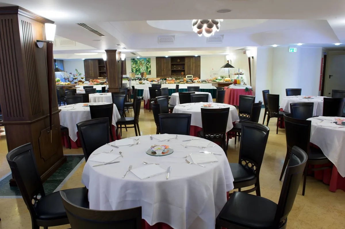 Sala ristorante con tavoli rotondi apparecchiati con tovaglie bianche e sedie scure