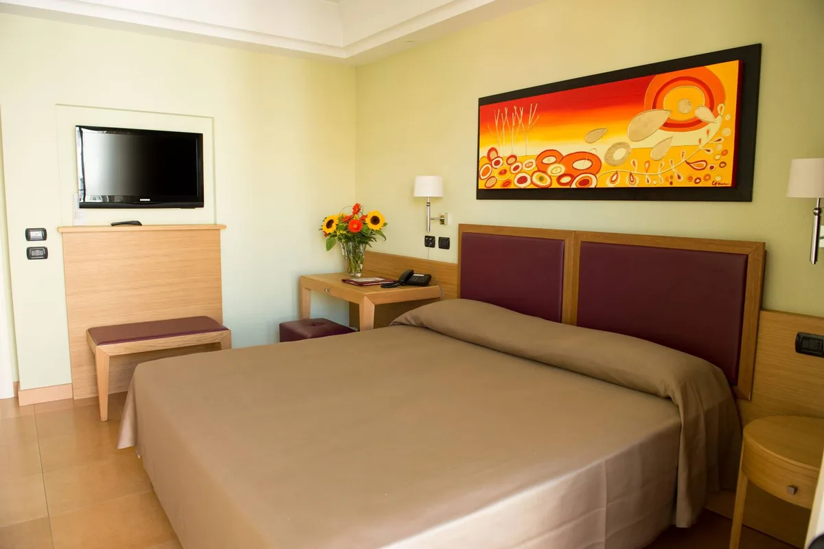Camera luminosa con letto matrimoniale, TV, scrivania e quadro colorato alle pareti