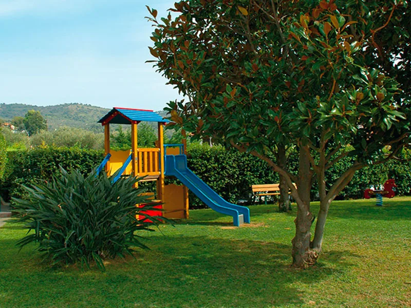 Area giochi per bambini con scivolo colorato nel giardino con alberi e siepi