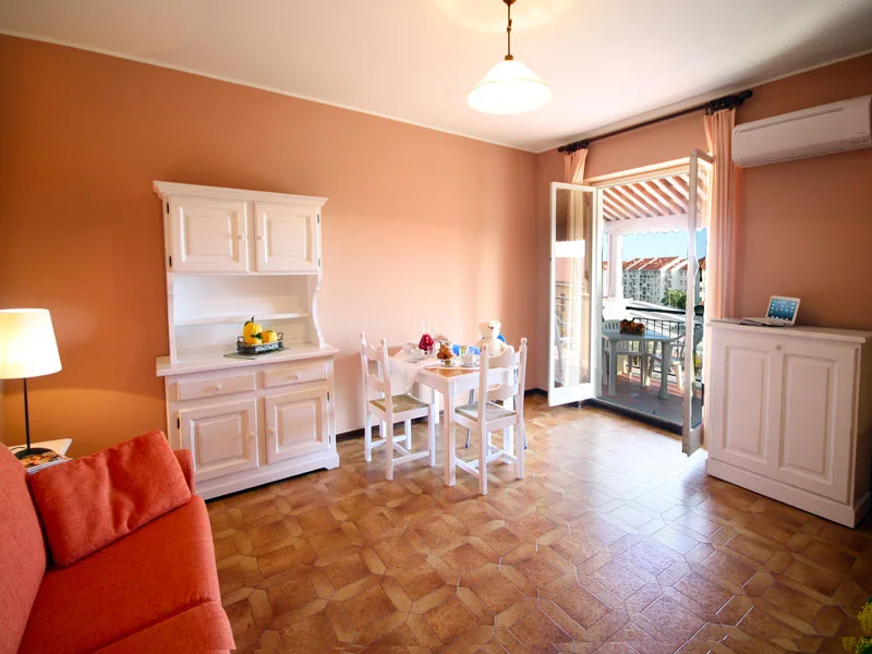 Soggiorno con pareti arancioni, credenza bianca, tavolo da pranzo e accesso al balcone