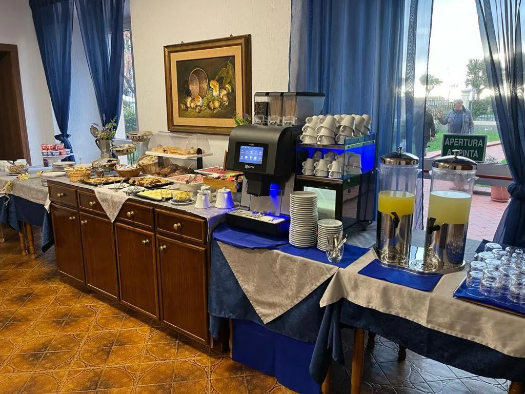 Buffet della colazione con dolci, salumi, macchina del caffè e dispenser di succhi su tavoli con tovaglie blu