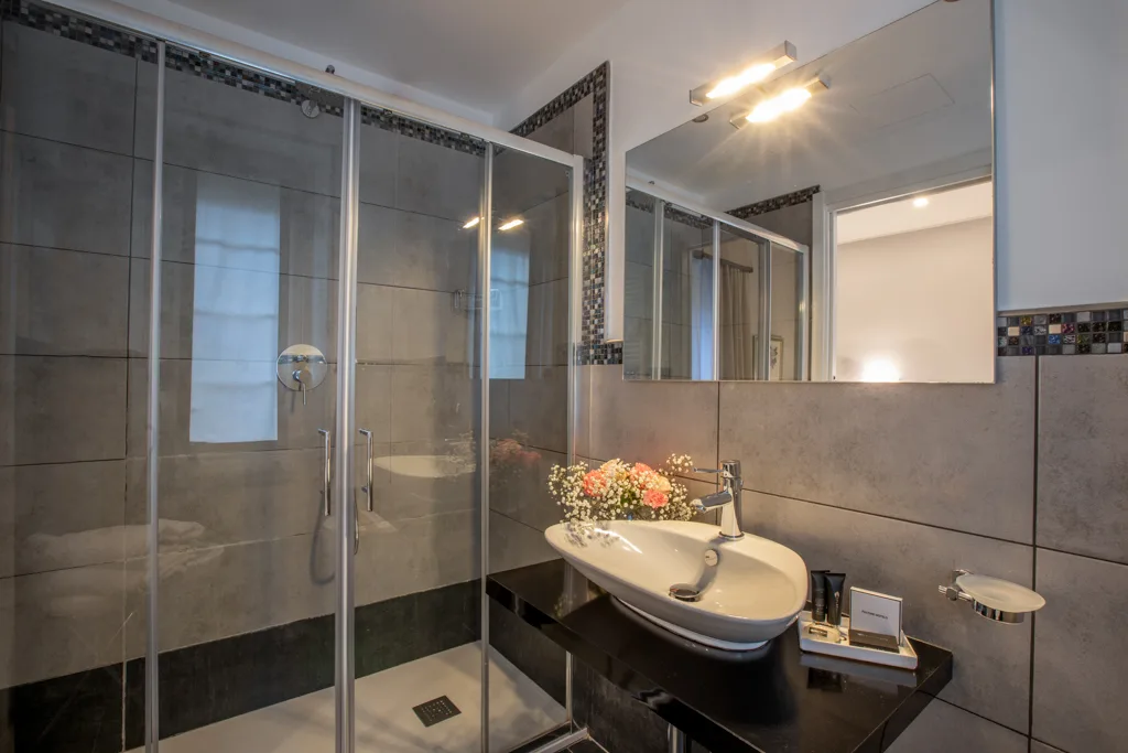 Bagno moderno con doccia in vetro, piastrelle grigie, lavabo da appoggio e specchio illuminato
