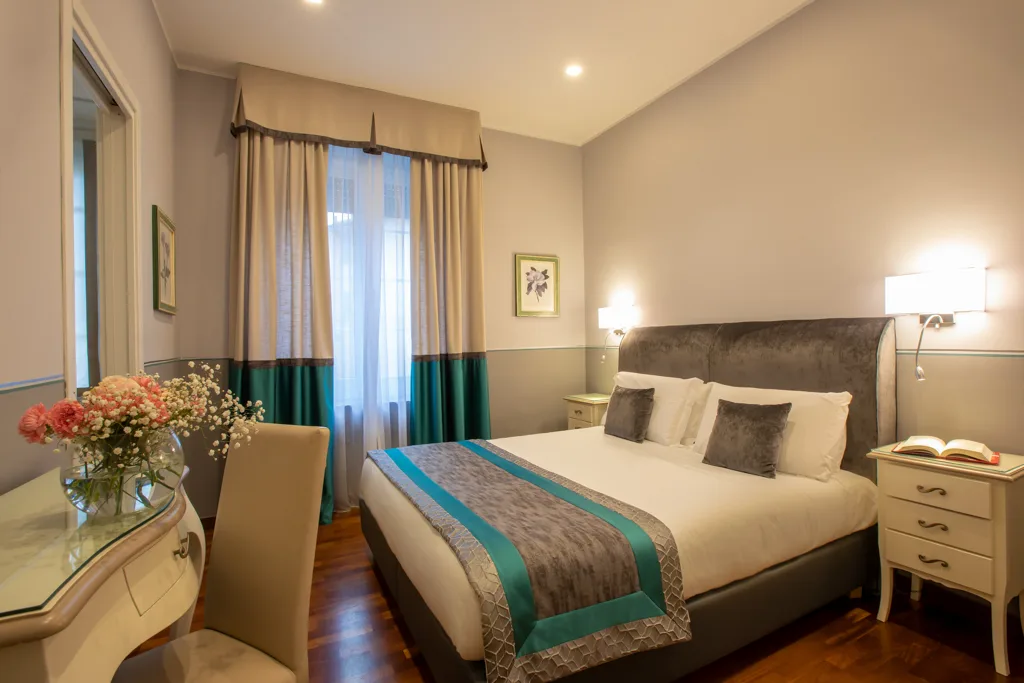 Camera elegante con letto matrimoniale, dettagli turchesi, scrivania con fiori e parquet in legno