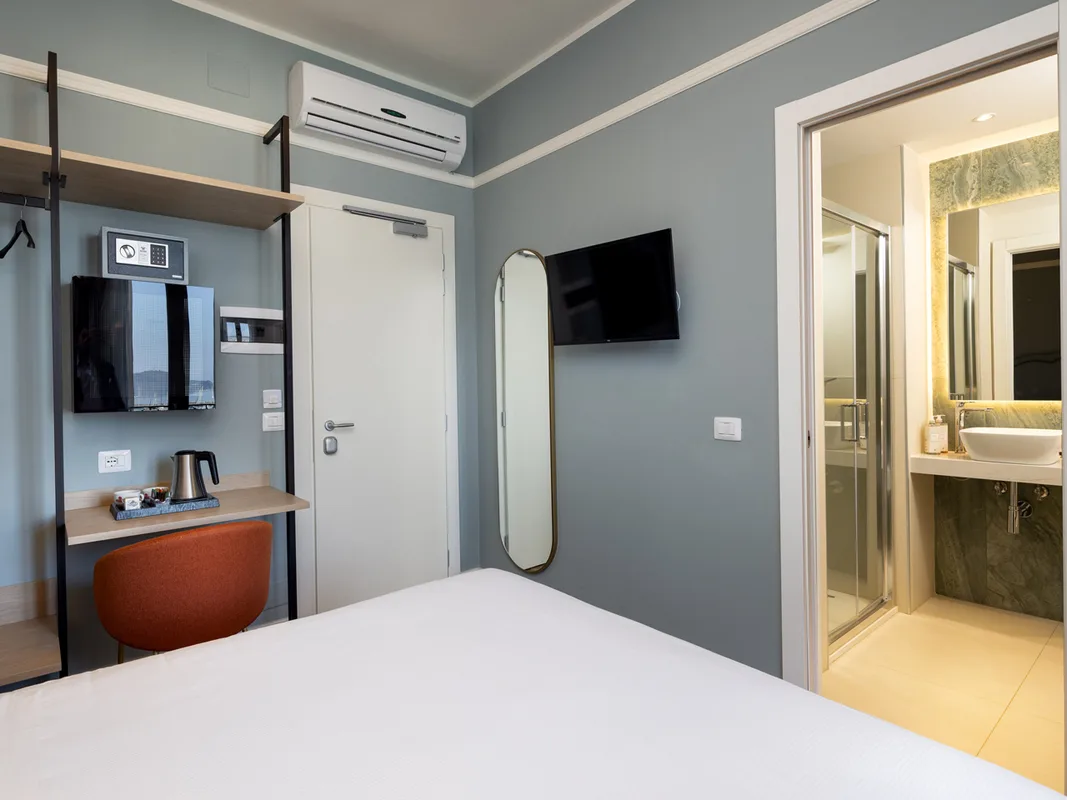 Dettaglio camera con scrivania, TV, cassaforte e bagno con doccia adiacente