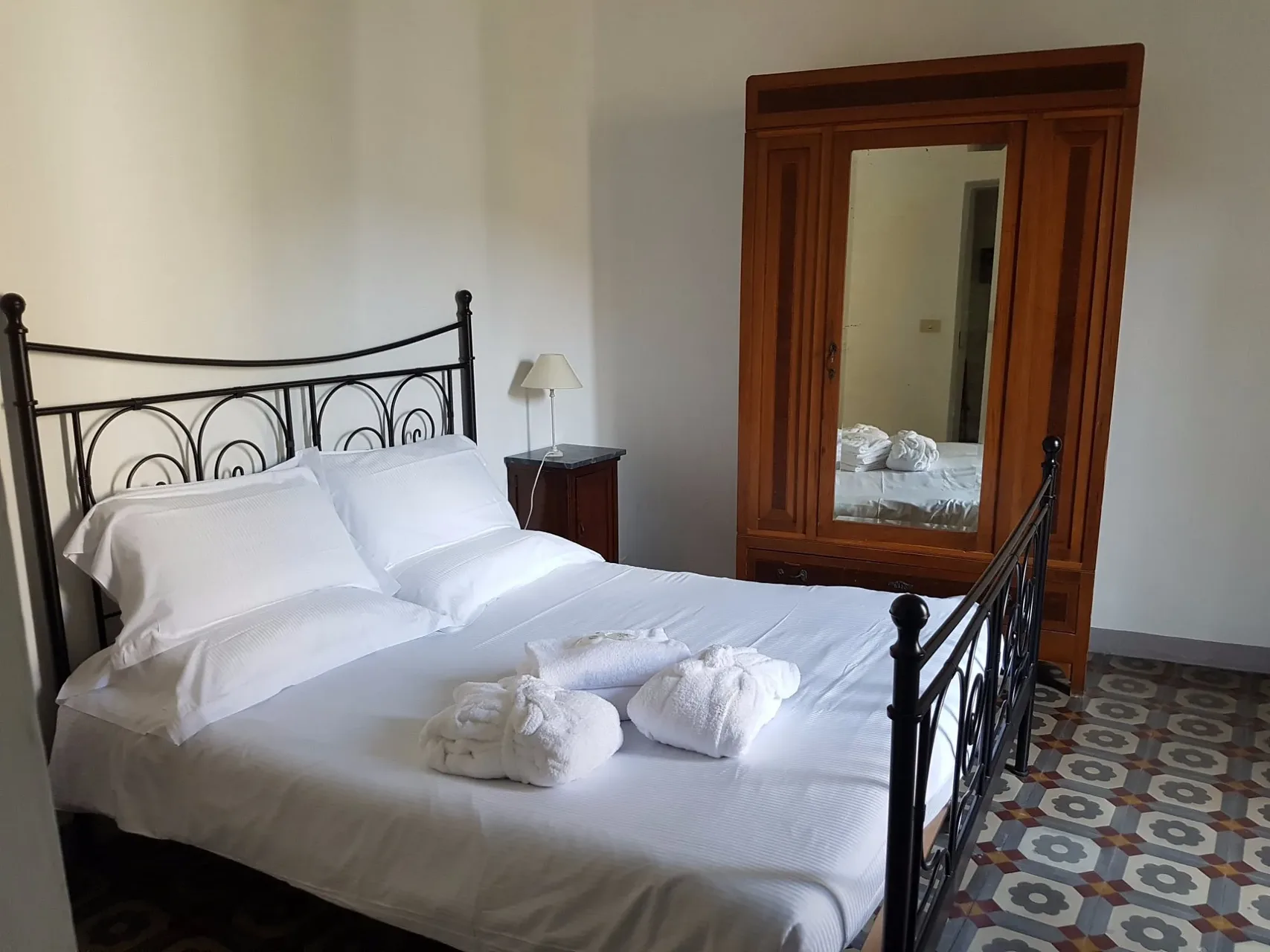 Camera matrimoniale con letto in ferro, armadio con specchio e pavimento decorato