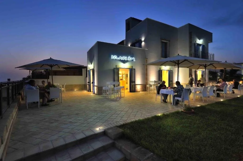 Lounge bar dell'hotel illuminato al tramonto con tavoli all'aperto e ombrelloni