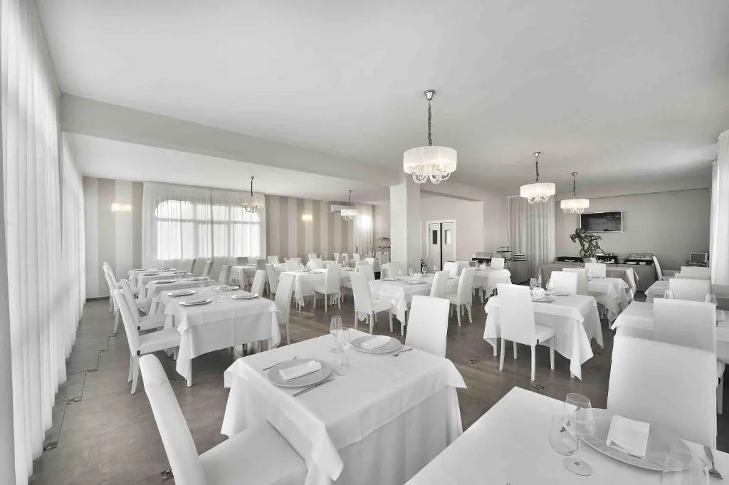 Ampia sala ristorante luminosa con tavoli vestiti di bianco e grandi tende