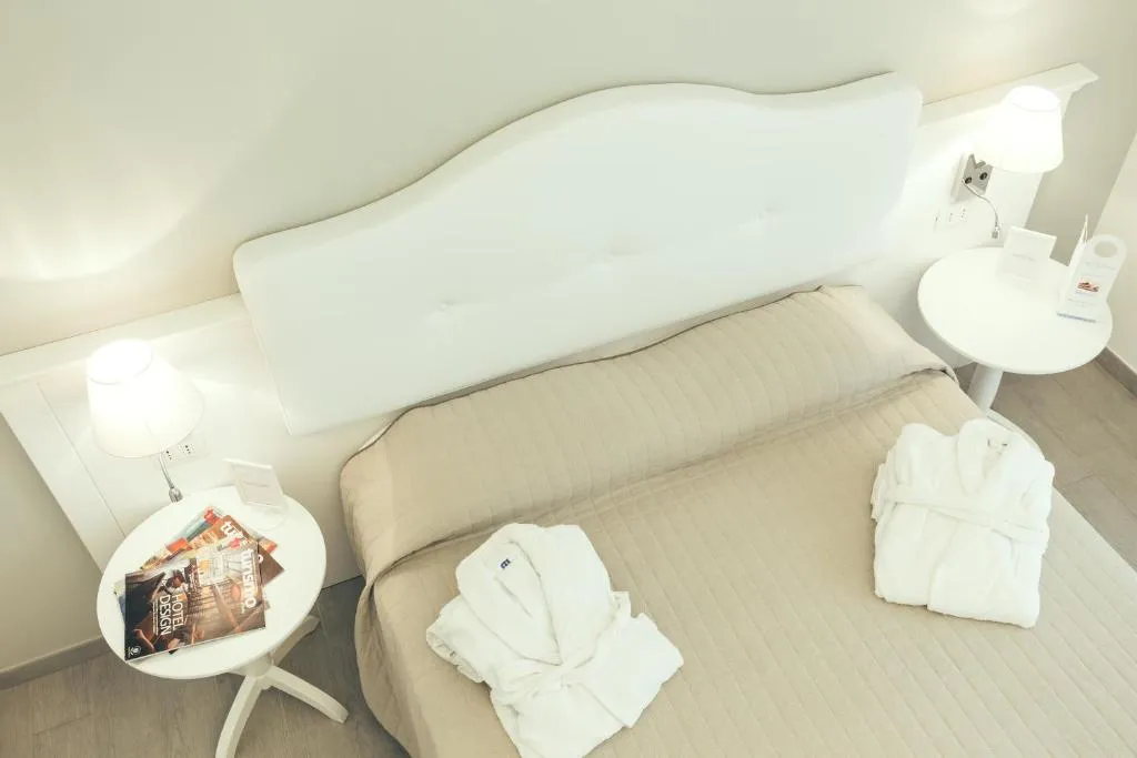 Dettaglio di letto con testiera bianca, accappatoi e comodini con lampade