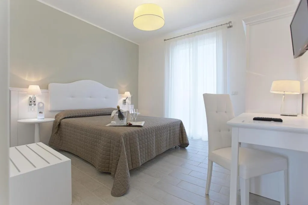Camera matrimoniale luminosa con letto, scrivania bianca e grande finestra con tende