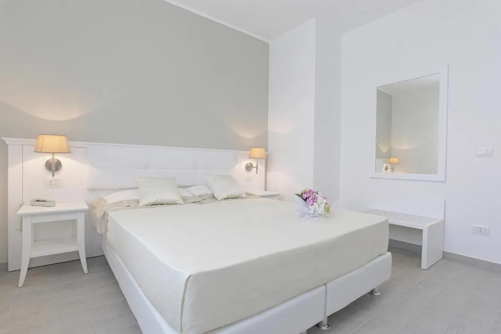 Camera matrimoniale bianca con letto, specchio e illuminazione soffusa