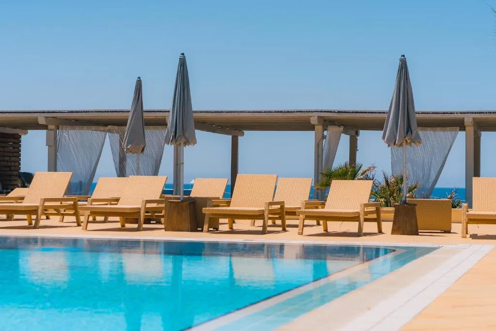 Bordo piscina con lettini in vimini e ombrelloni grigi affacciati sul mare