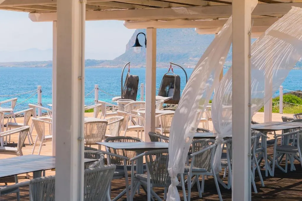 Terrazza coperta con tavoli, sedie bianche e tende svolazzanti vista mare