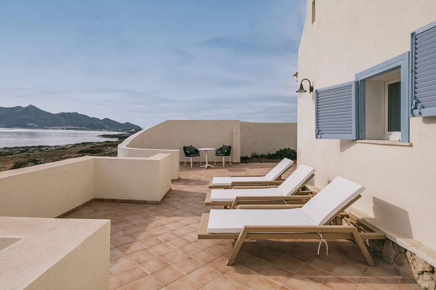 Terrazza privata con lettini bianchi e tavolino vista mare e montagne