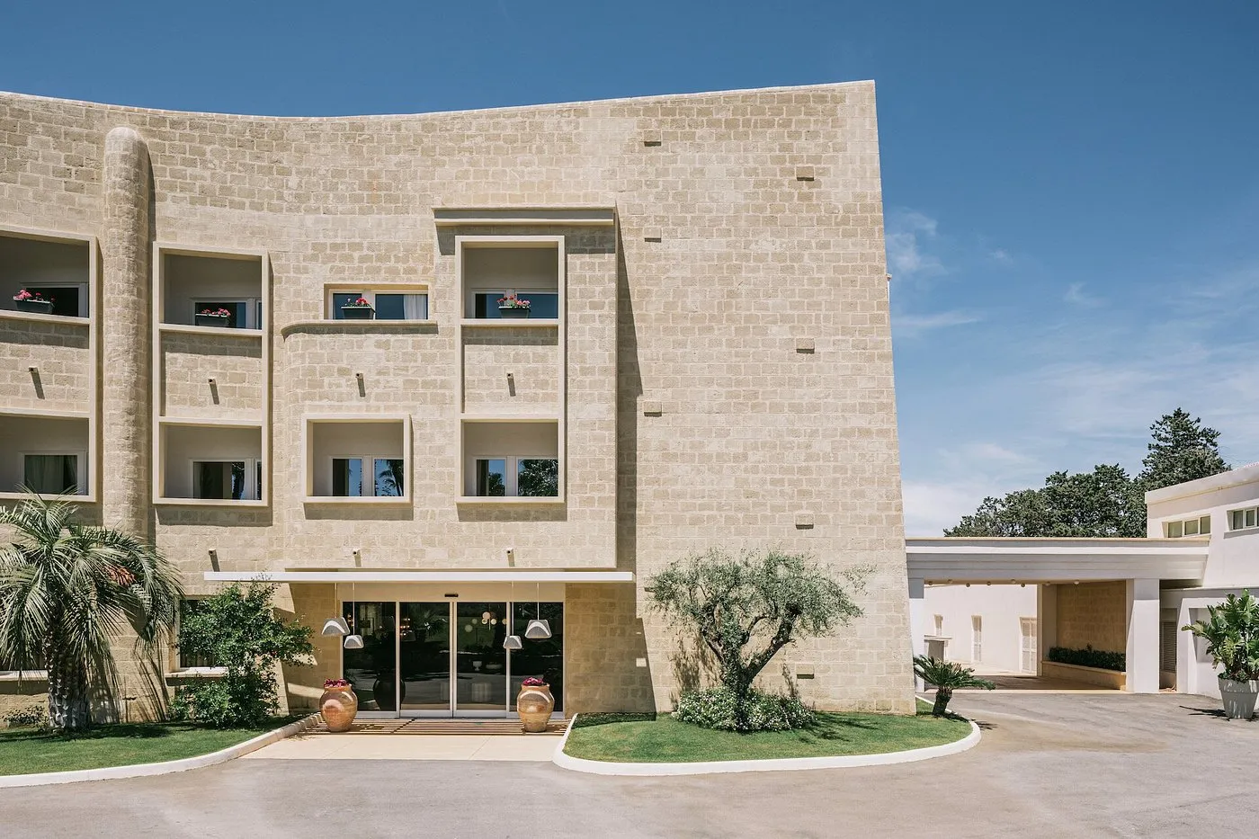 Facciata in pietra chiara dell'hotel con ingresso e ulivo davanti