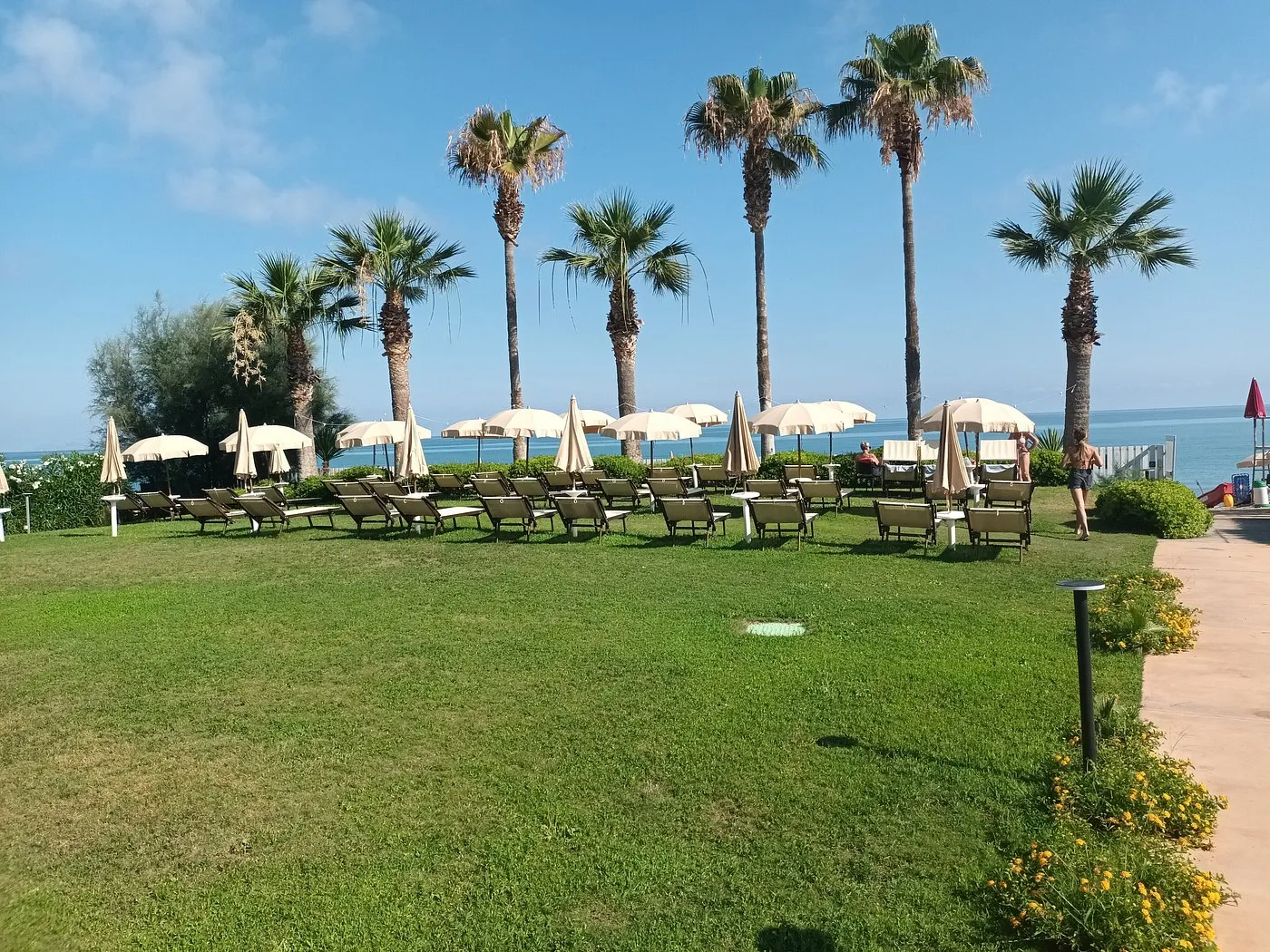Giardino con lettini e ombrelloni beige tra le palme affacciato sul mare