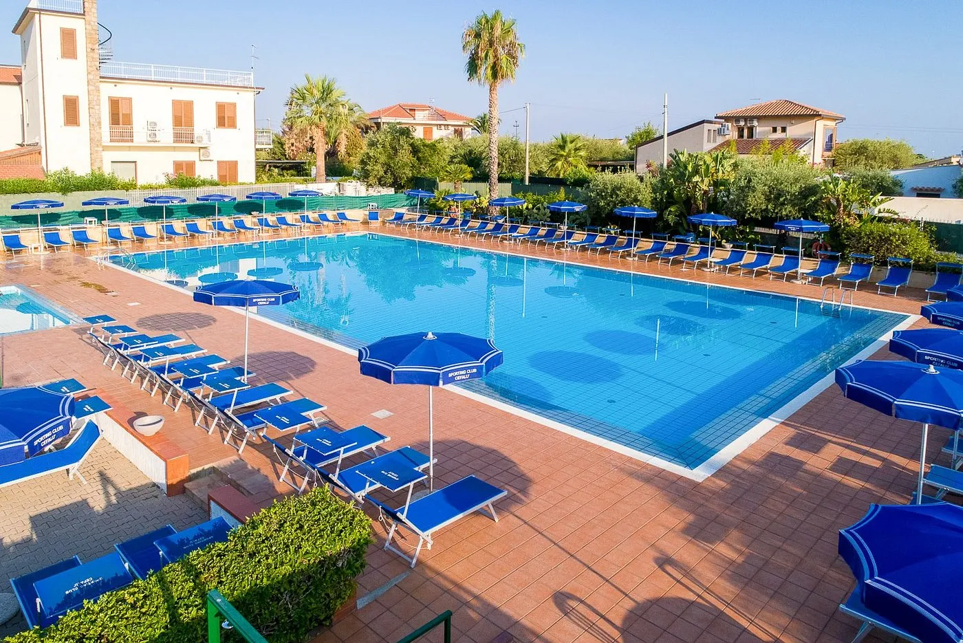 Piscina con pavimentazione in cotto, lettini e ombrelloni blu Sporting Club Cefalù