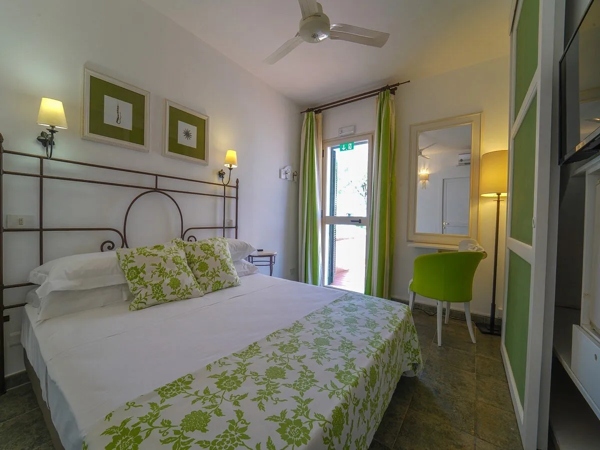 Camera luminosa con letto matrimoniale, tende verdi e accesso al terrazzo