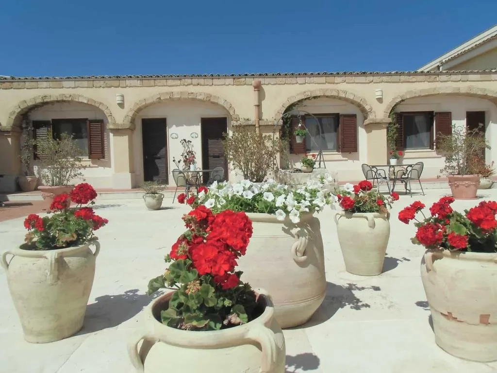 Cortile soleggiato con grandi vasi di gerani rossi e petunie bianche davanti a edificio con archi in pietra